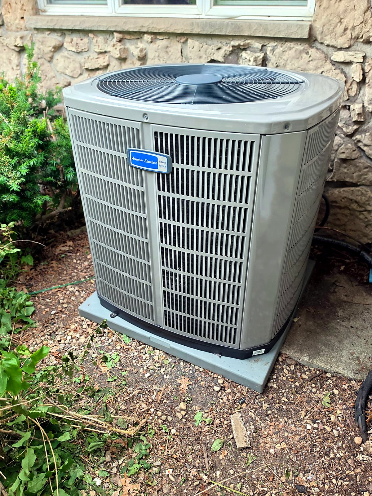 American Standard air conditioner installed beside a stone home